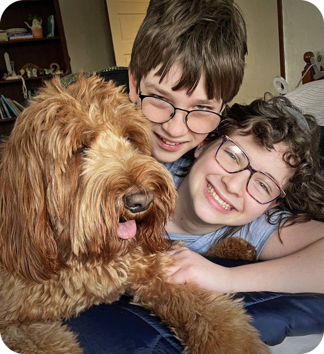 Two bespectacled brothers smile with their Doodle dog.