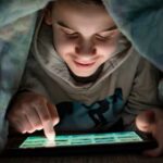 Child using tablet in bed under the covers
