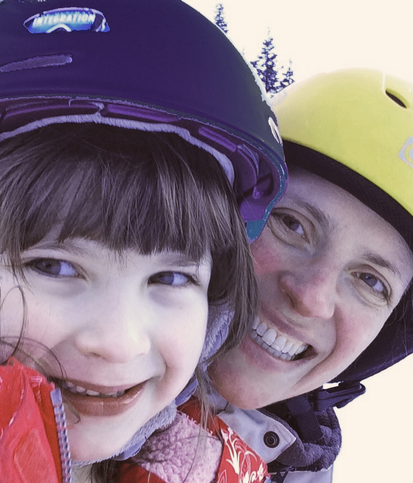 Mother and daughter in ski helmets and skiing attire smiling on a ski slope