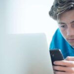 boy looking at phone in front of laptop