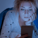 Girl looking at phone under blanket in dark