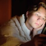 boy looking at phone in dark on bed