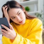 Woman with head in hand looking at phone because of parental control app scam on iPhone