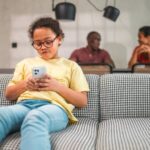 Young girl watching YouTube on phone while parents sit at table in background