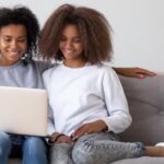 mother and daughter looking at laptop together on couch