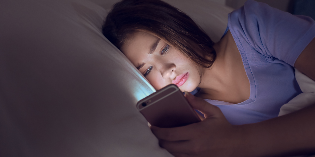 Teen looking at phone on bed in dark